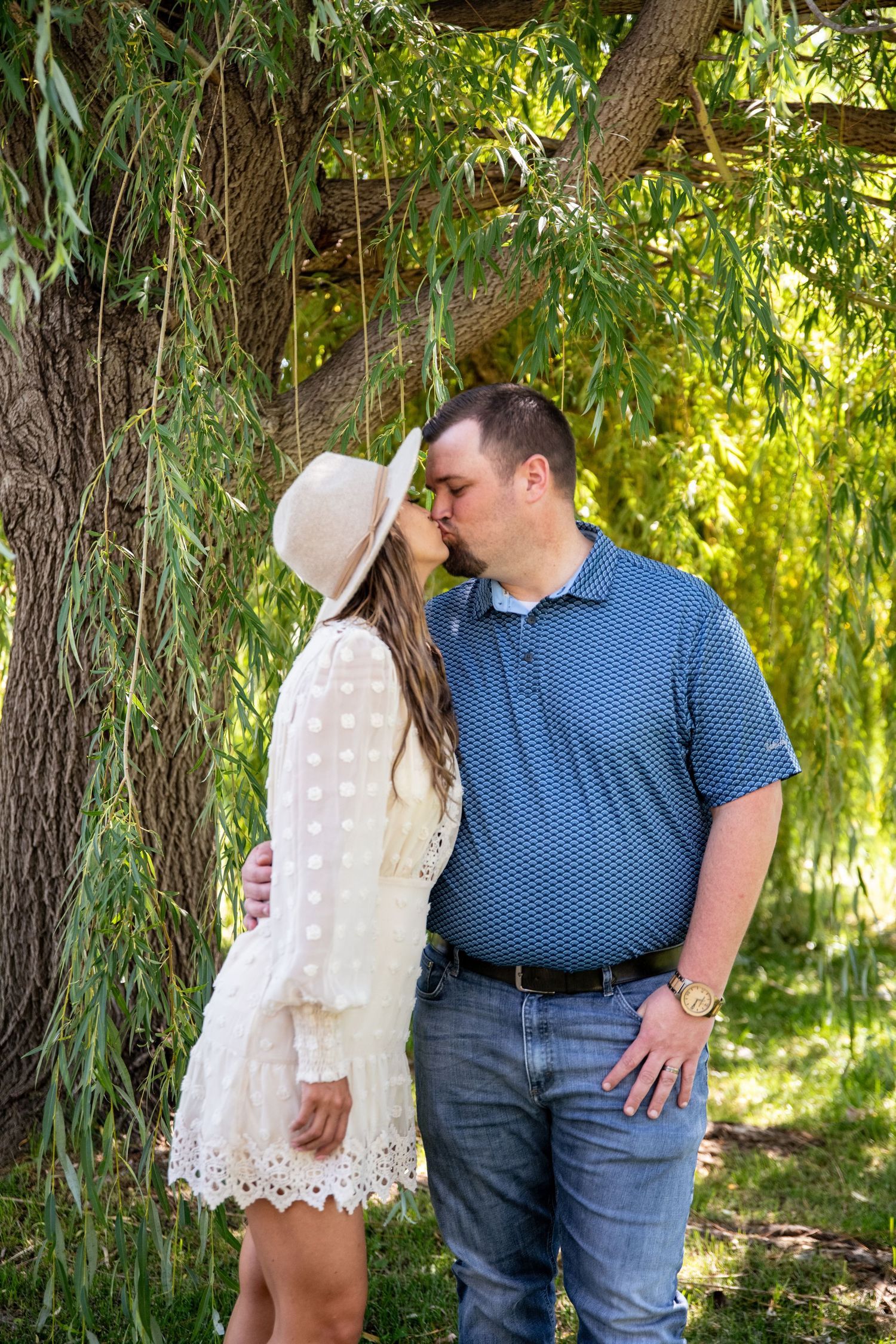 Romantic couple sharing intimate moment under weeping willow trees in park.