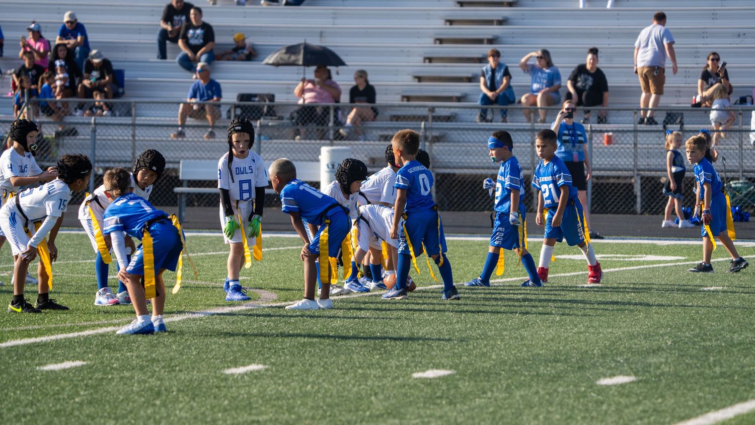 Soccer players perform stretching exercises on a sports field during warmup with coaches observing nearby.