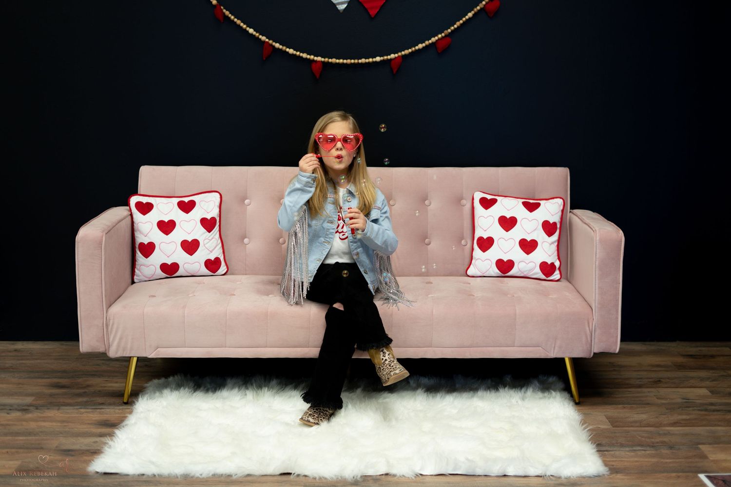 Pink sofa with heart pillows against dark wall with Valentine's Day decorations.