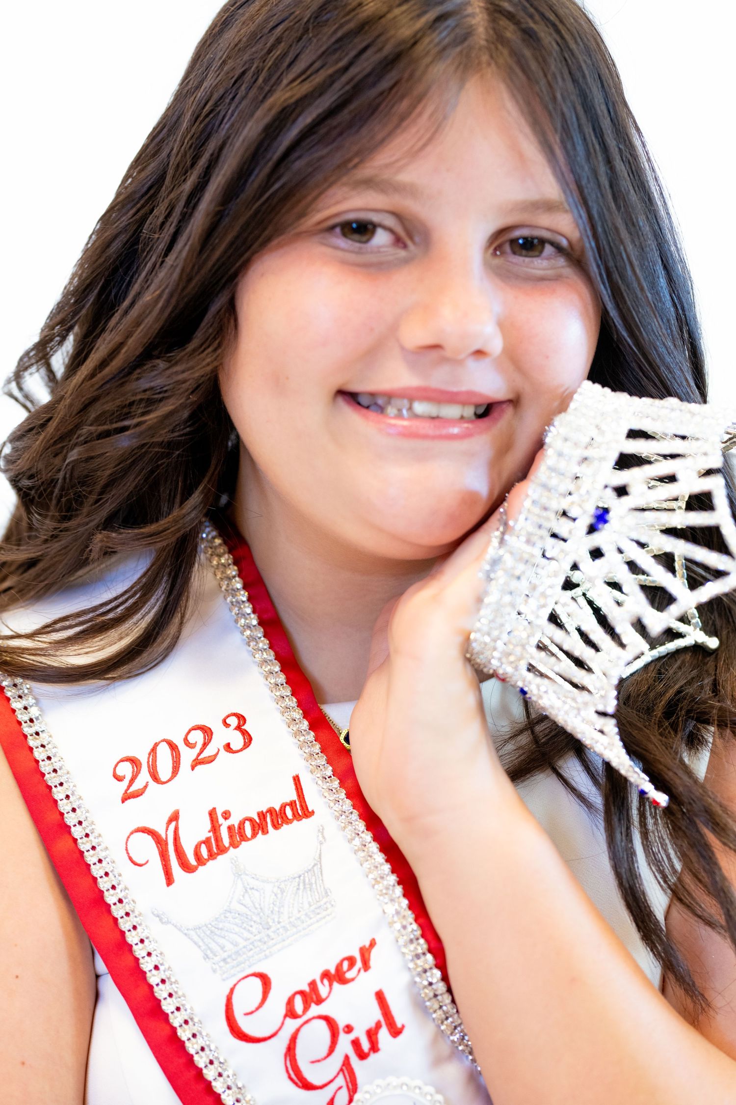 A pageant winner wearing a 2023 National Cover Girl sash poses with a crown.