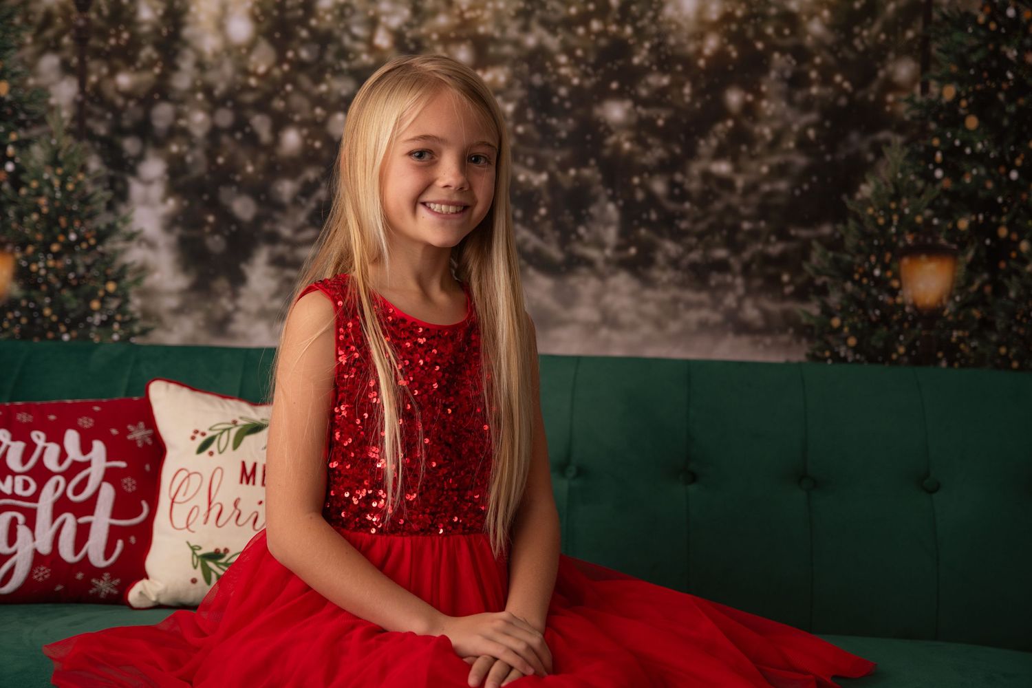 A child in a sparkly red dress sits on a green couch with Christmas decorations.