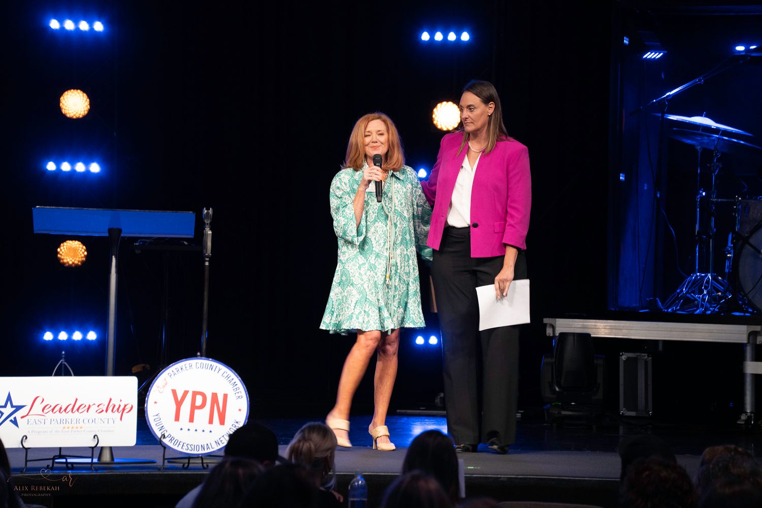 Two speakers present on stage with professional lighting and event backdrop.