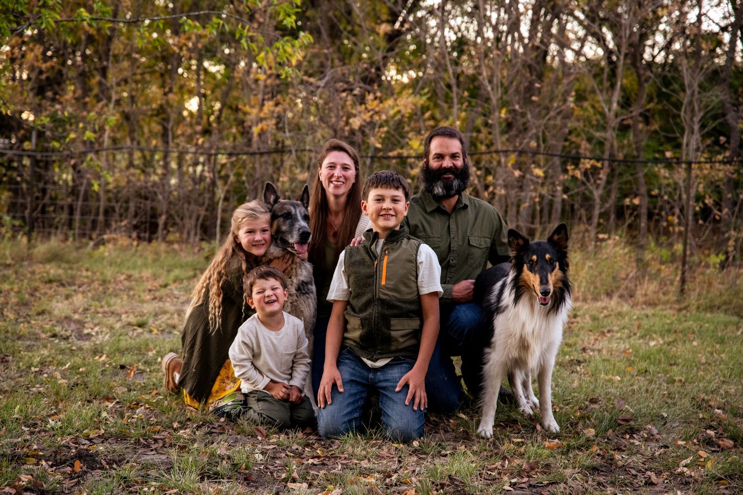 Family portrait with dog outdoors in autumn setting with fall foliage.