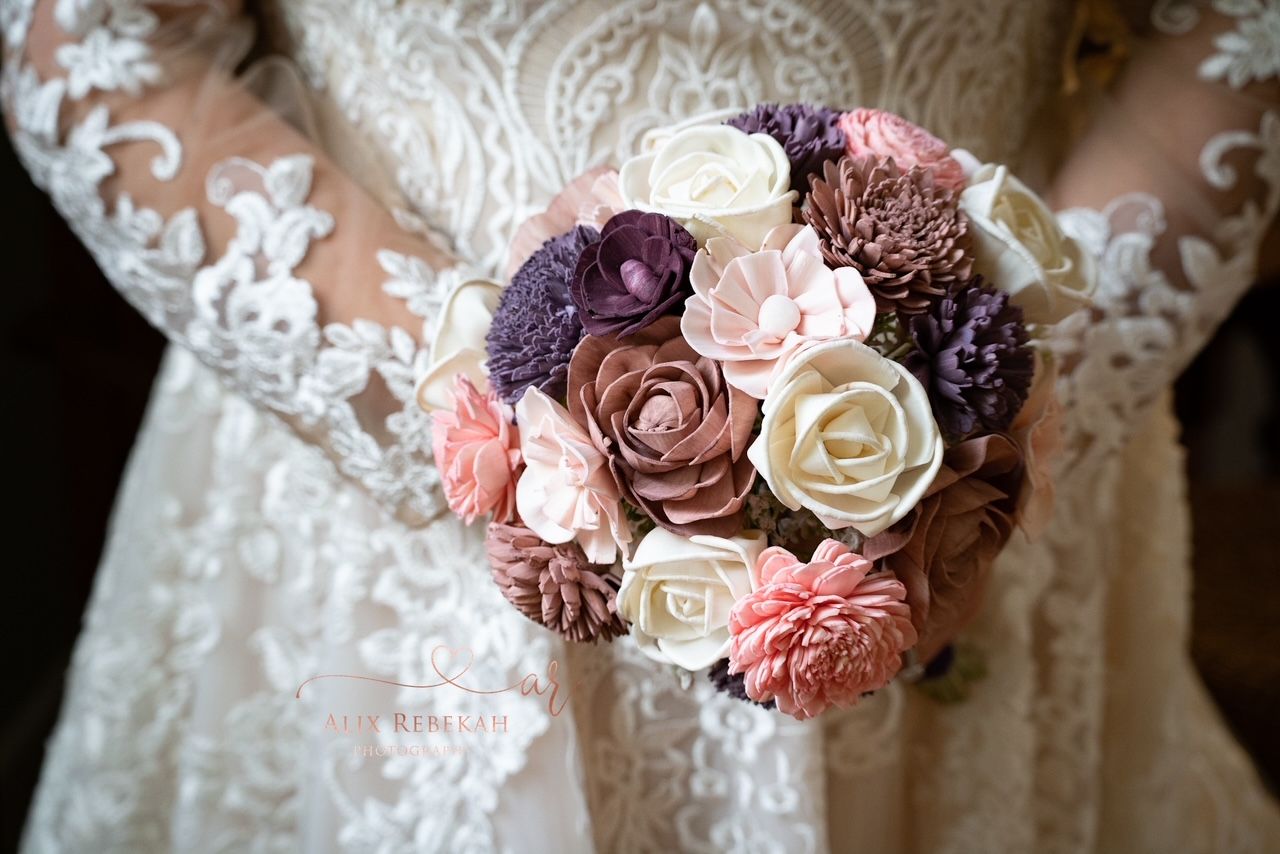 A delicate bridal bouquet featuring purple, pink and white roses against lace fabric.
