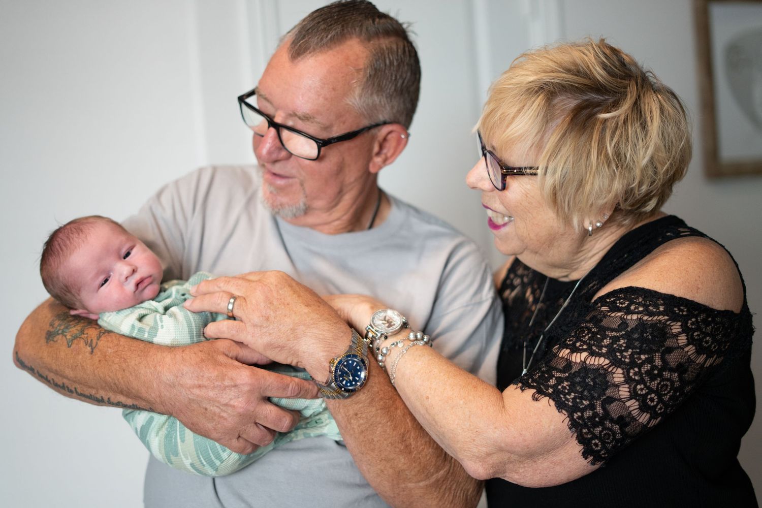 Grandparents hold and gaze lovingly at their newborn grandchild during a family photo.