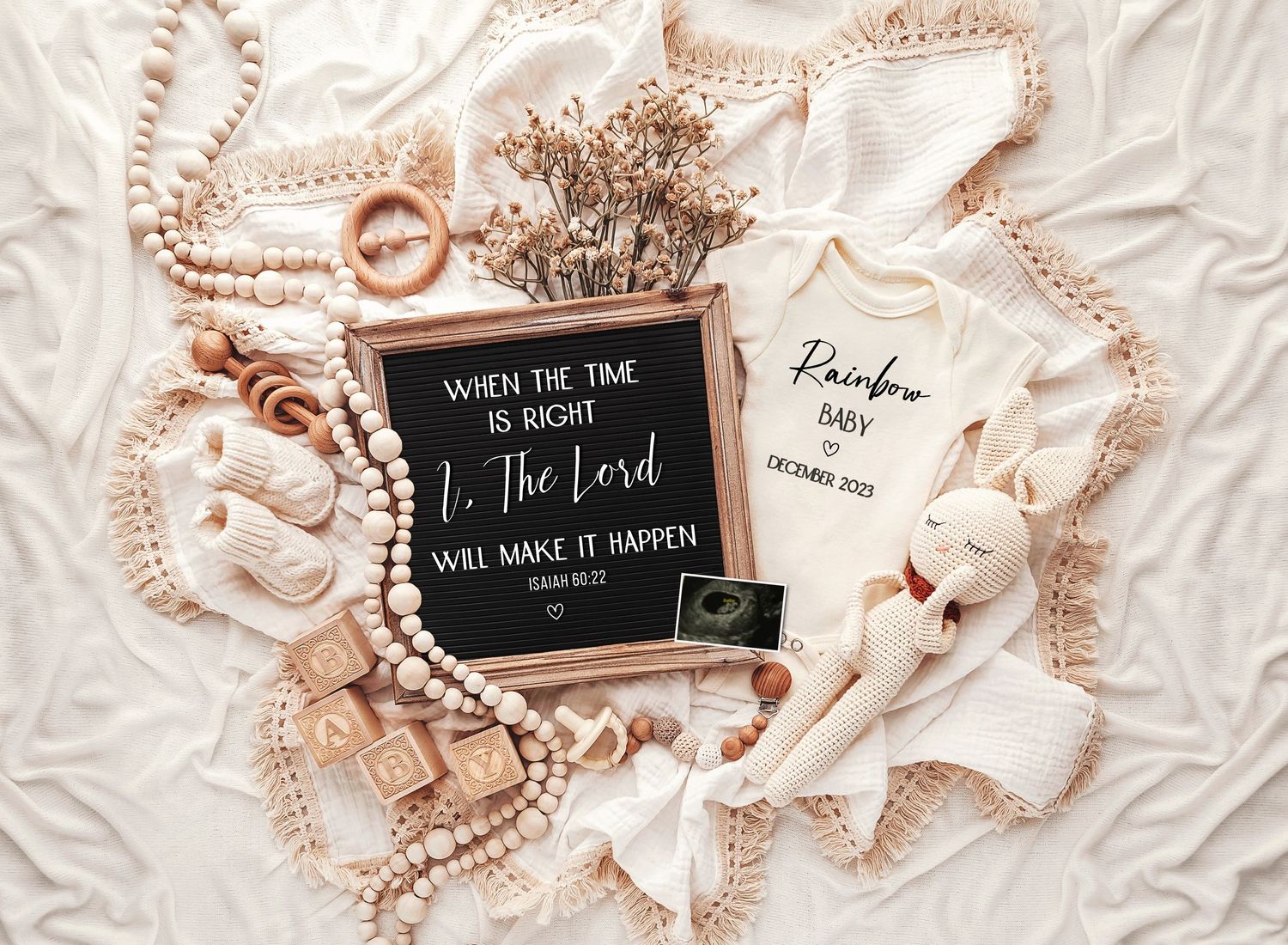 Flatlay of baby announcement items with letter board and pearl decorations on white fabric.