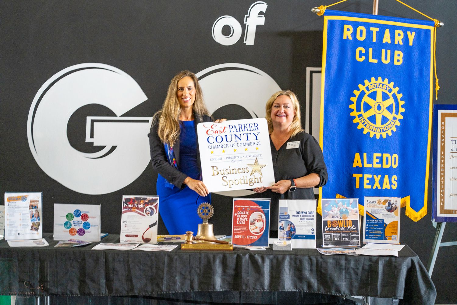 Chamber members present award certificate at Rotary Club event with branded banner display.