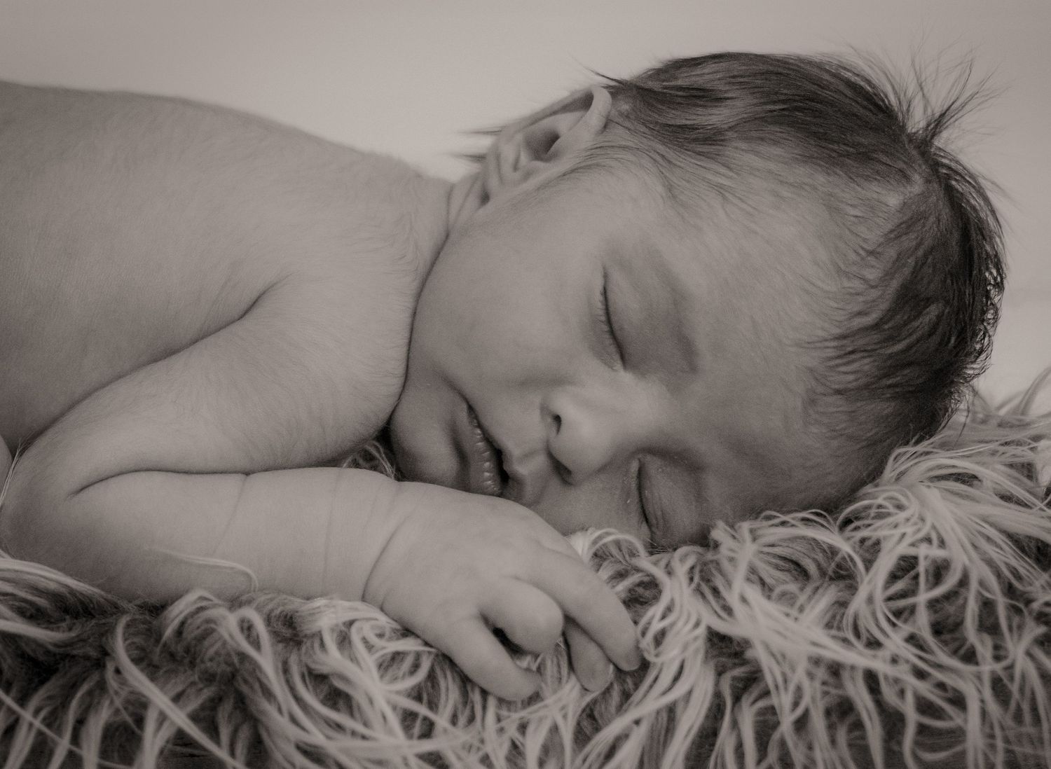 A black and white portrait of a sleeping baby on soft furry texture.