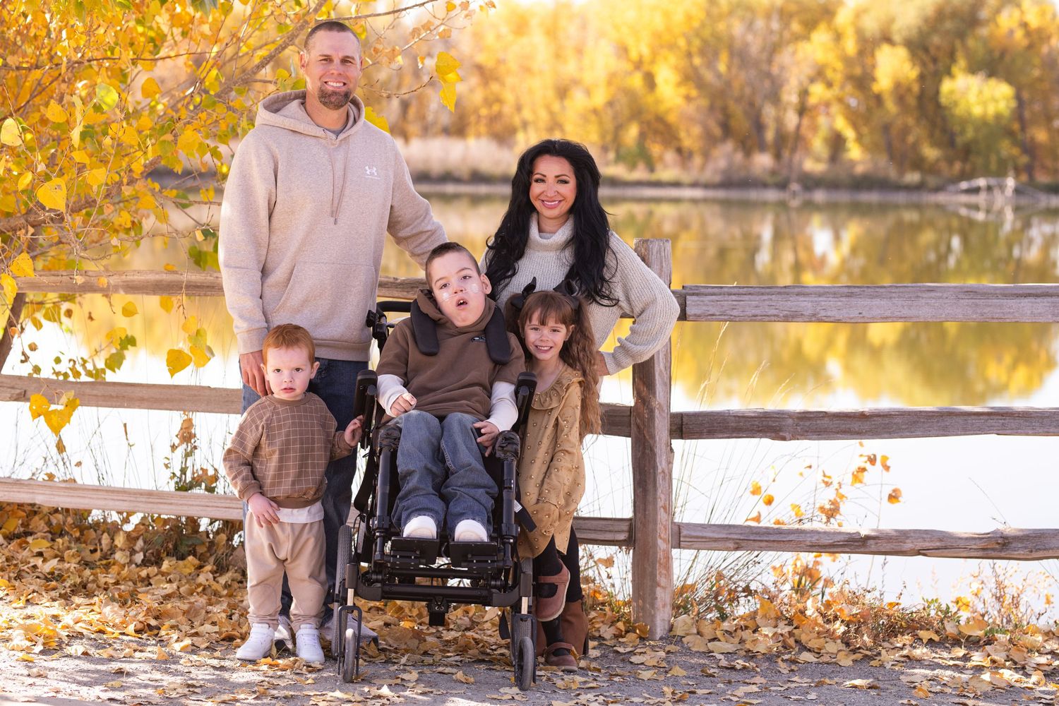 Family group photo in autumn setting with colorful fall foliage by a lake.