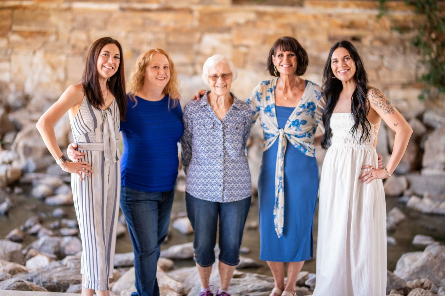 Multi-generational family group posing together against stone wall backdrop.