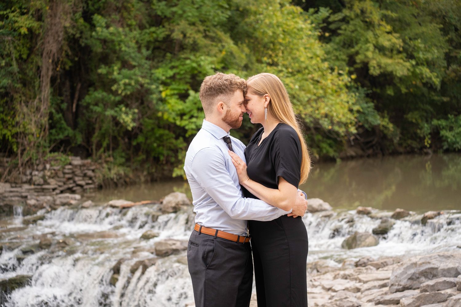 Couple shares romantic moments by a cascading waterfall in a lush forest landscape during an engagement photoshoot.