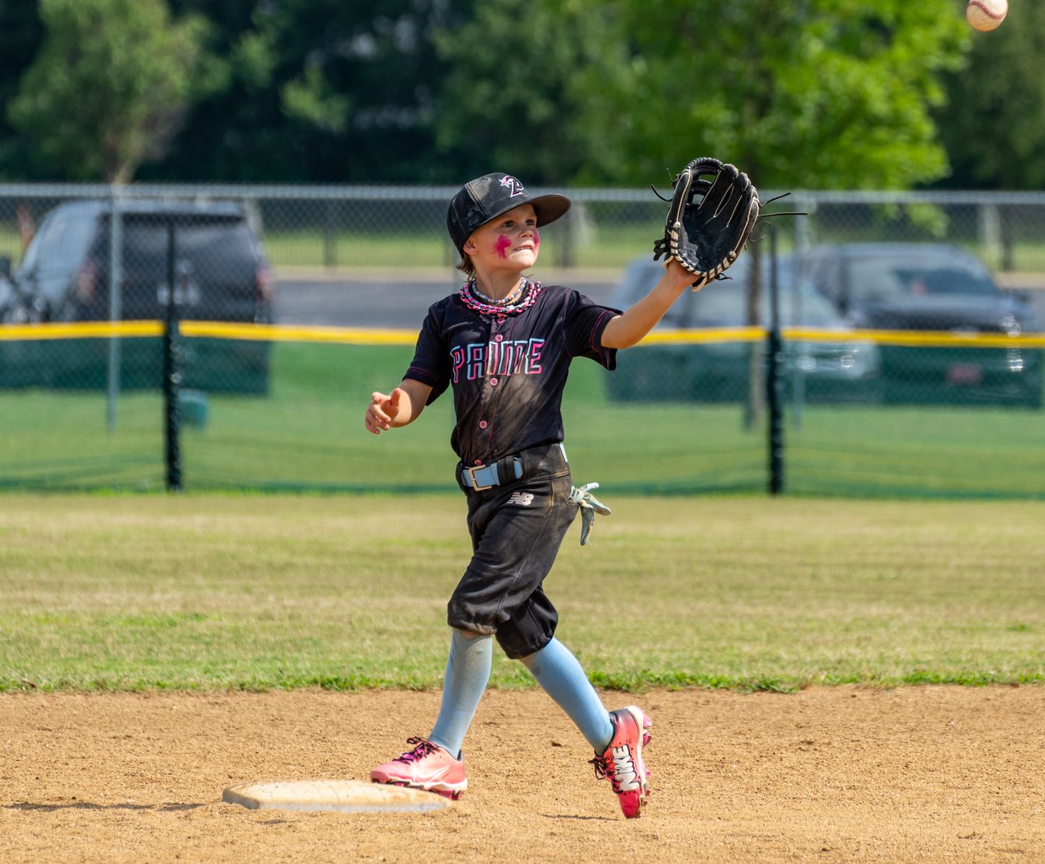 Young baseball player in black uniform catching a ball on the field during a youth league game on a sunny day.