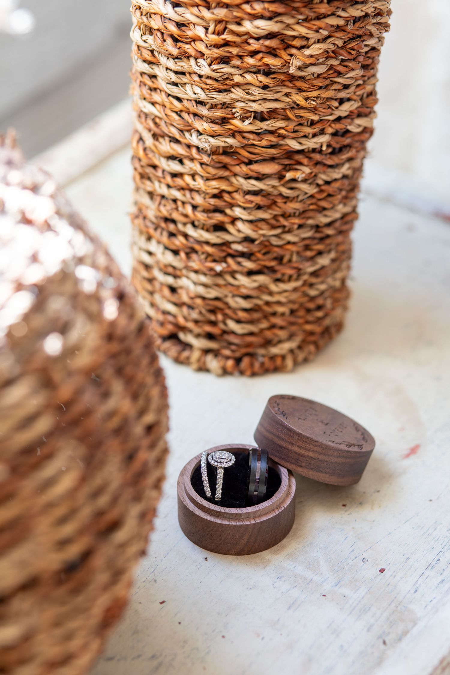 Diamond engagement ring in wooden box beside woven wicker baskets on white surface.