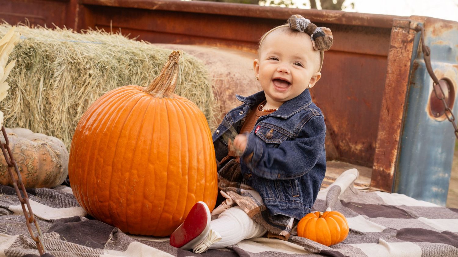 Happy toddler sits next to large orange pumpkins on rustic wooden surface.