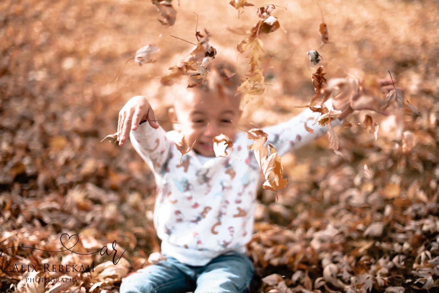 Child playing and throwing autumn leaves in the air during fall season.