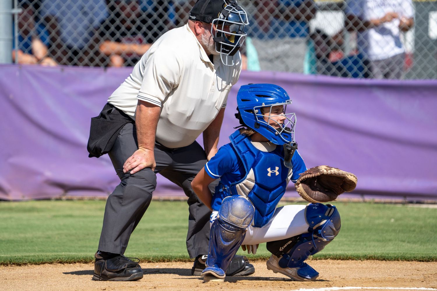 Baseball umpire and catcher in protective gear crouched behind home plate during game.
