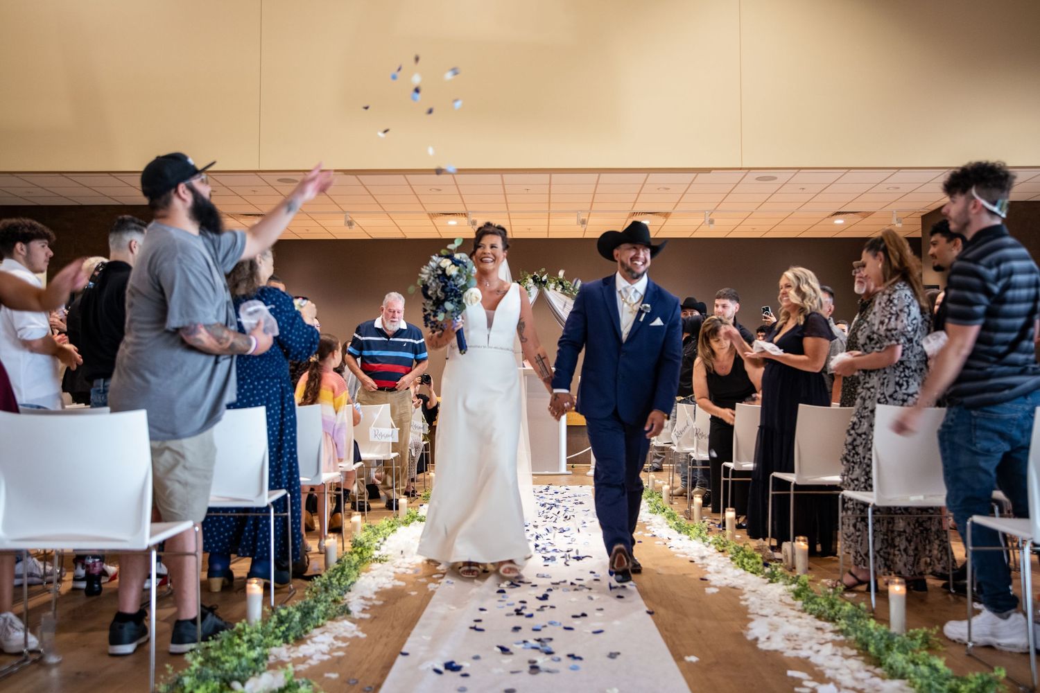 A celebration at a wedding ceremony with guests tossing confetti along a petal-lined aisle.