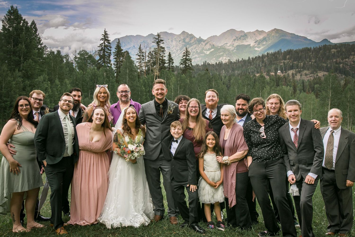 Large wedding party group photo with mountain landscape backdrop.