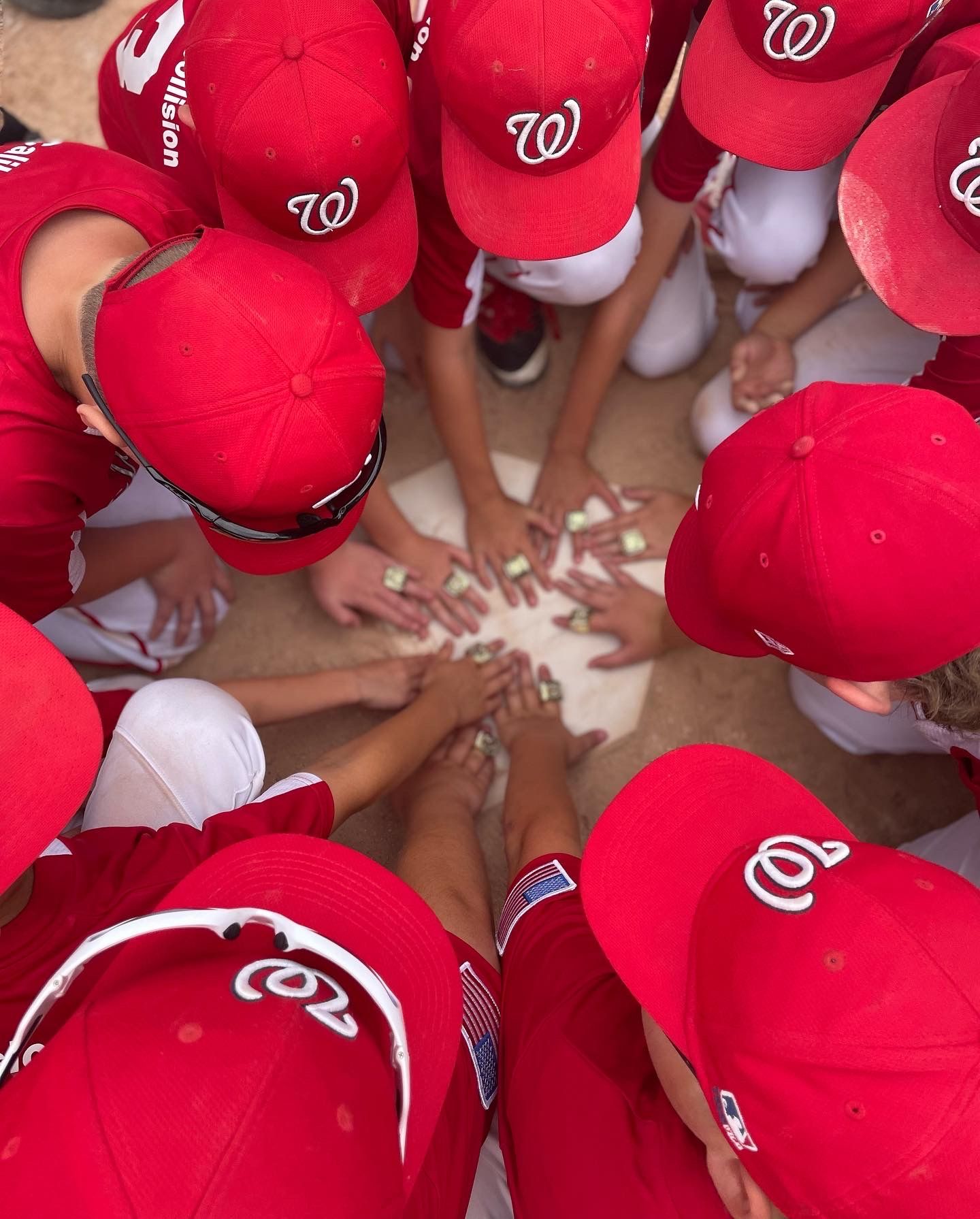 A huddle of baseball players wearing red Washington Nationals caps join hands in a pre-game team circle.