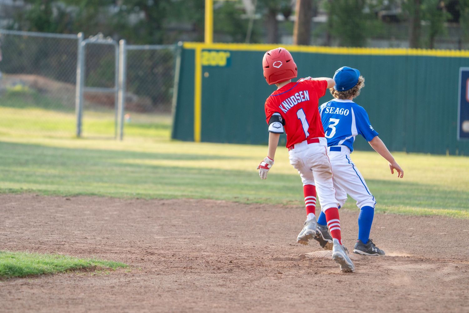 Baseball player in a red uniform slides safely into base as defensive player in blue attempts to make the tag.
