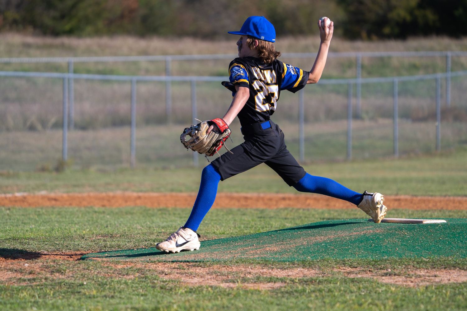 Baseball player in black jersey and blue pants winds up to throw a pitch from the pitcher's mound.