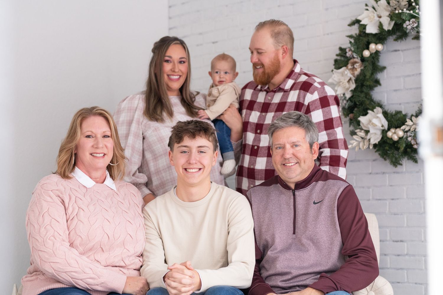 Family members wearing coordinated pink and burgundy outfits pose together against a white brick wall backdrop.