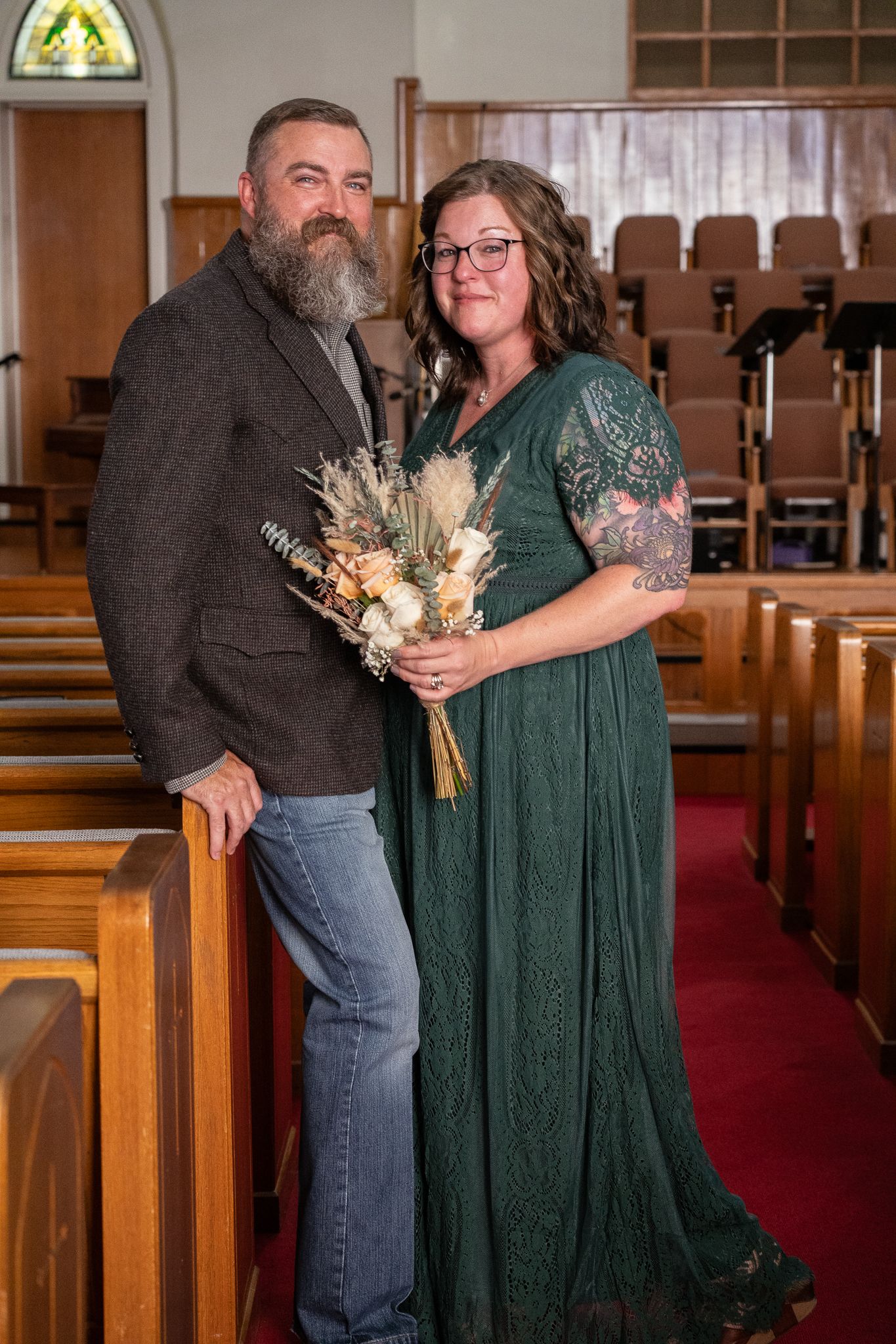 Couple posing in church pews with dried flower bouquet.