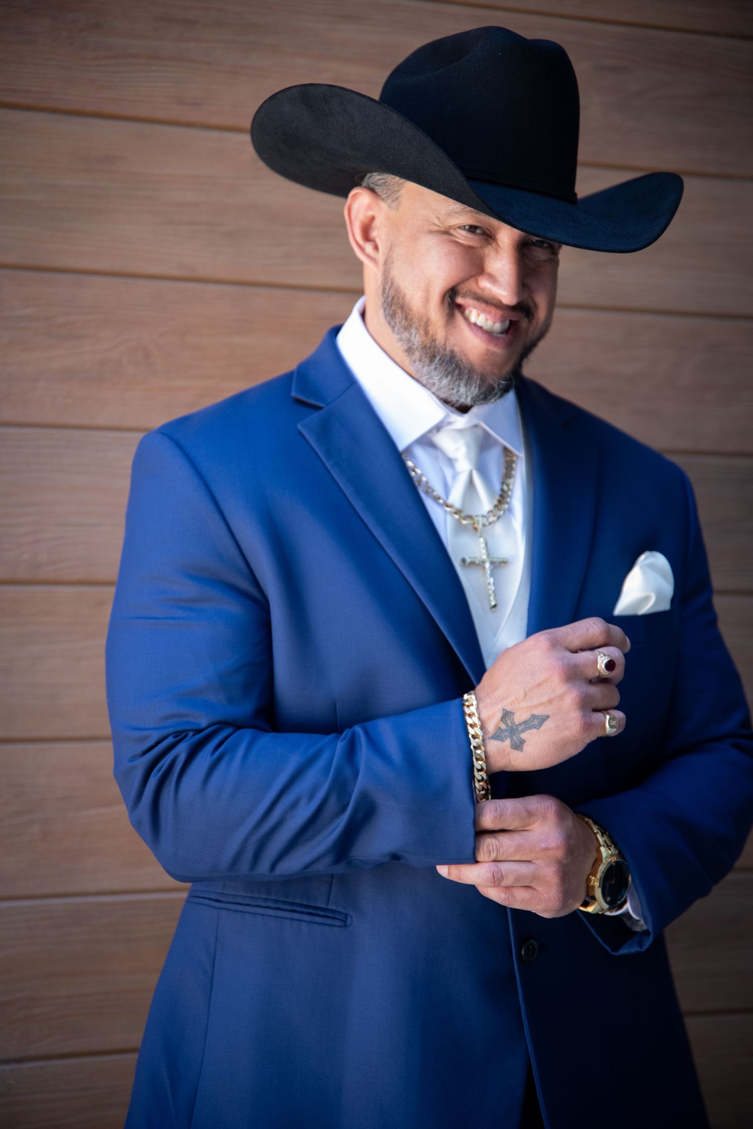 Groom in royal blue suit and black cowboy hat posing against wooden wall.
