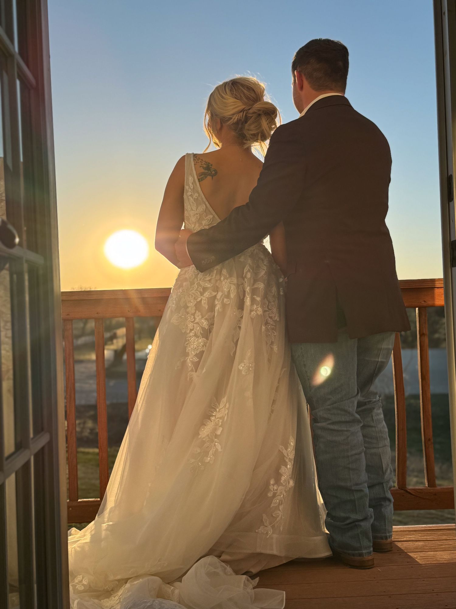 A couple in wedding attire silhouetted against a stunning golden sunset on a porch.