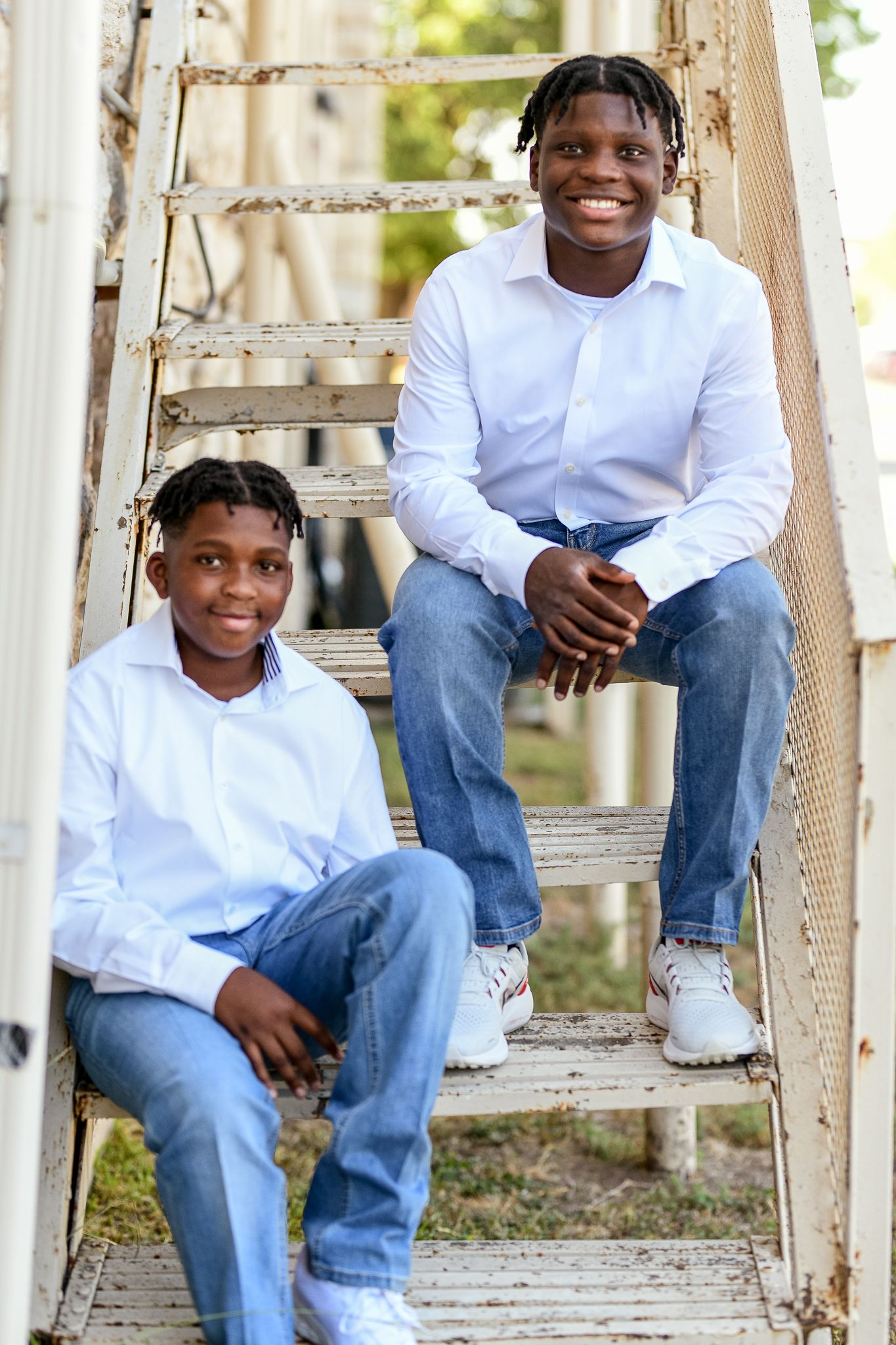 Two people sitting on weathered white wooden stairs outdoors.