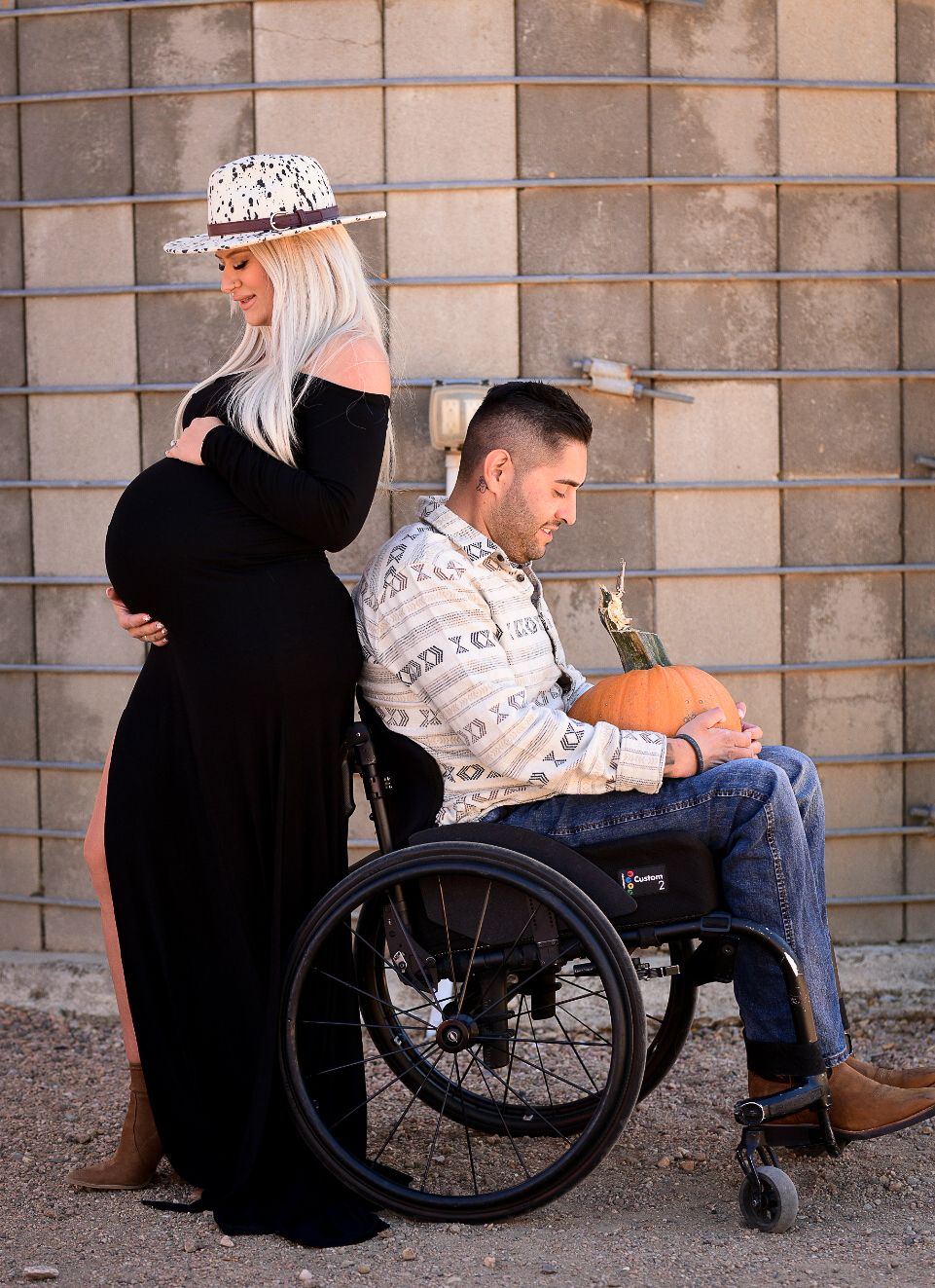 A couple poses together, with one person in a wheelchair, during a maternity photoshoot.