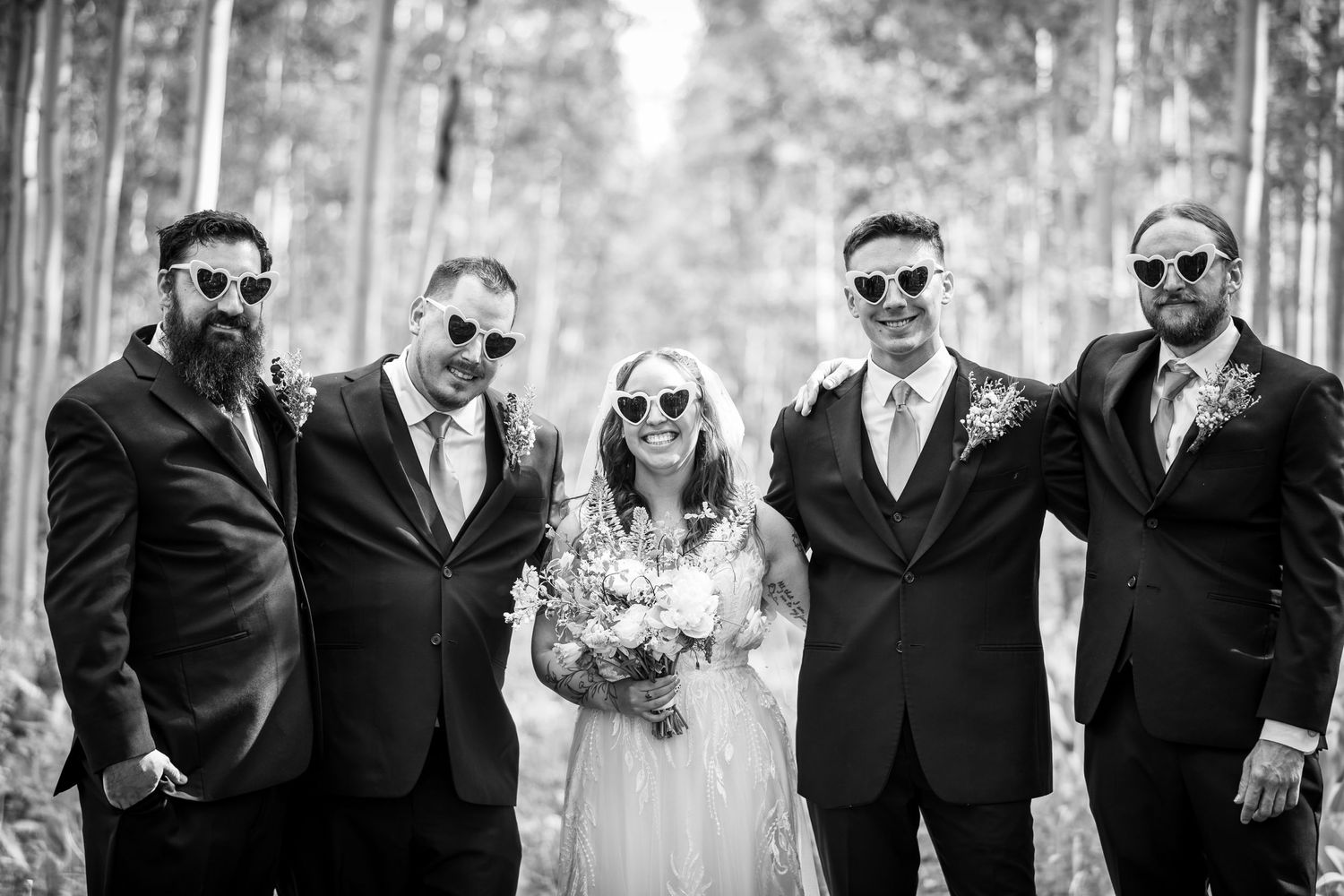 Wedding party in formal attire poses in black and white among aspen trees.