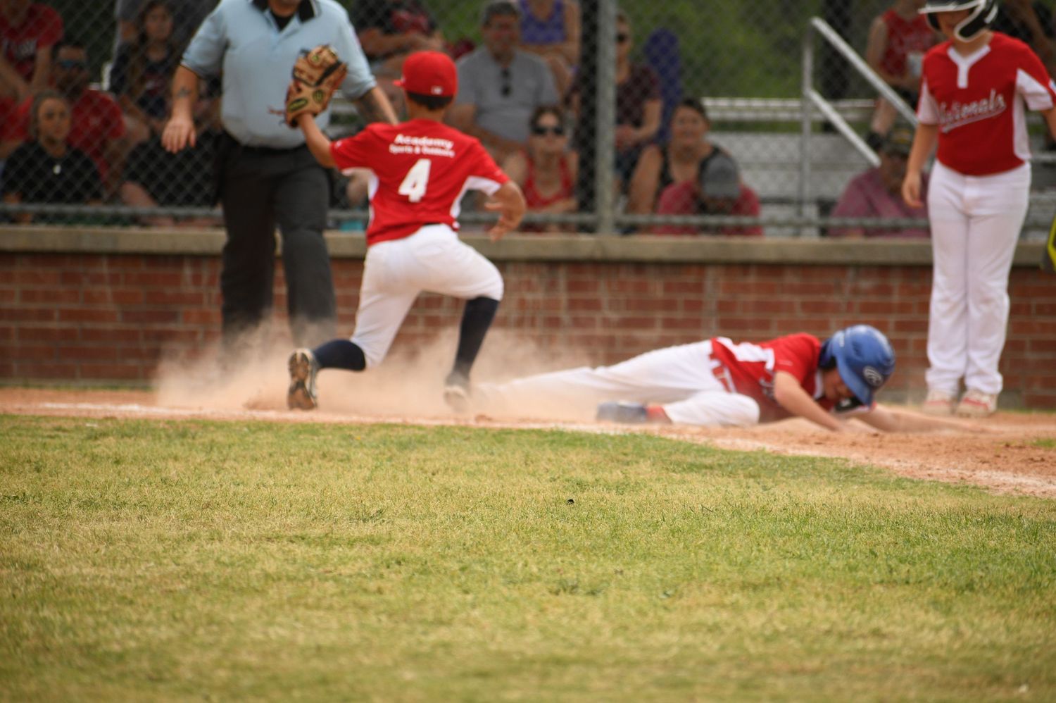 Baseball player in red uniform slides into base during competitive game on dusty diamond field.
