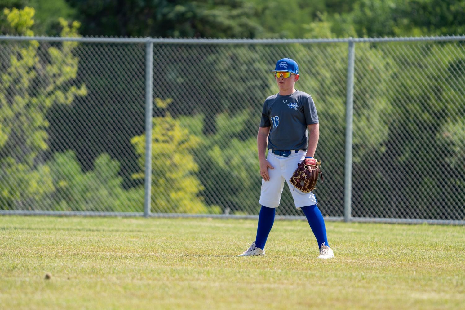 Baseball player in navy jersey and blue baseball cap stands ready in outfield position during game.