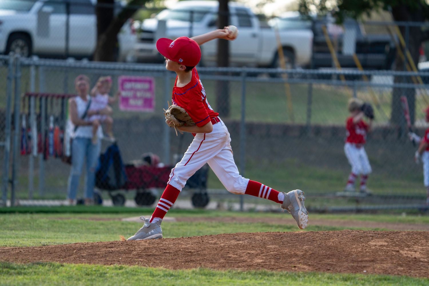 Youth baseball pitcher in red uniform follows through on delivery motion during Little League game.