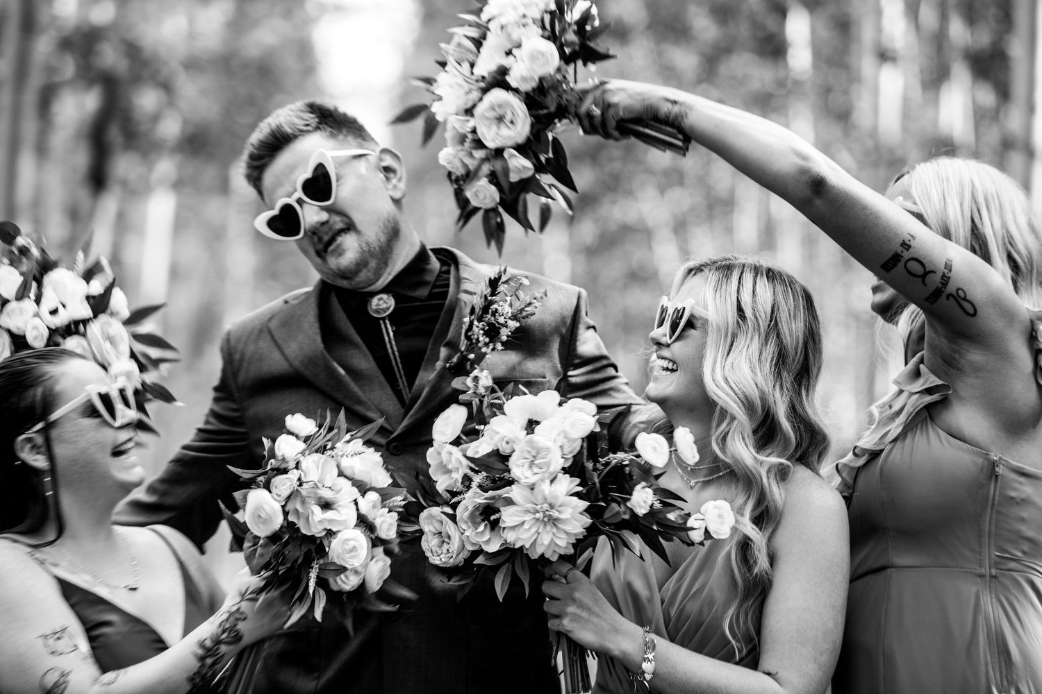 Black and white candid shot of wedding party celebrating with flower bouquets.