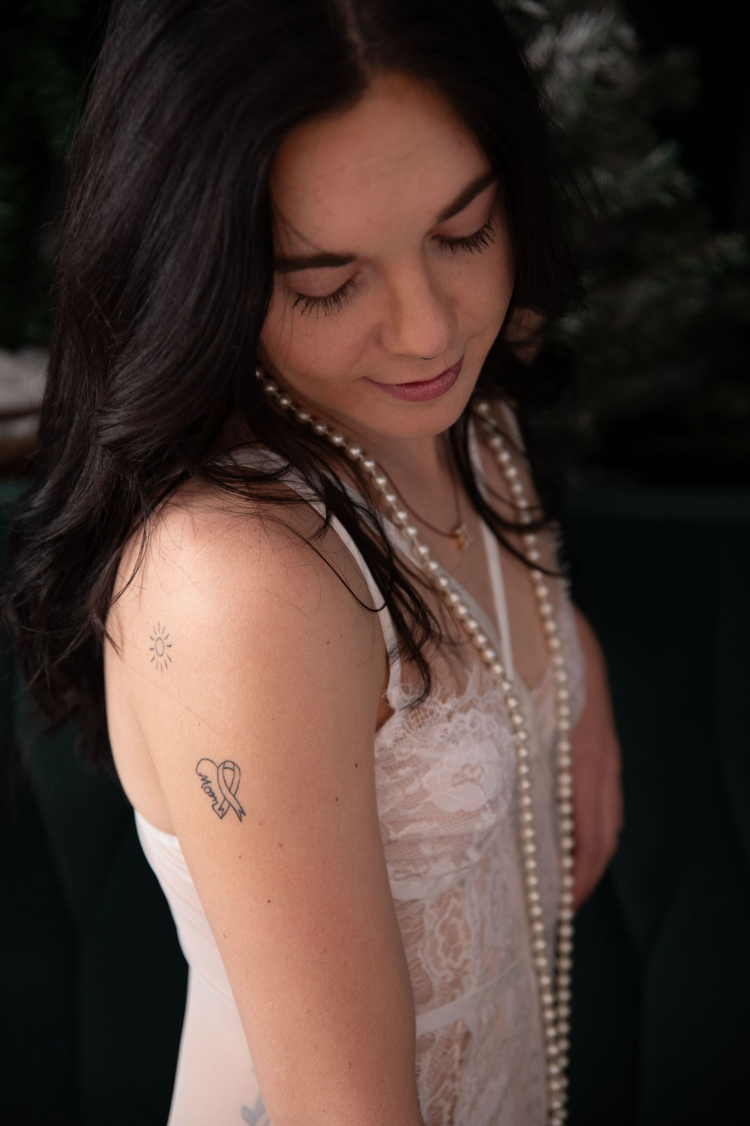 Elegant portrait featuring pearl necklaces and a delicate white lace top with visible butterfly tattoo.