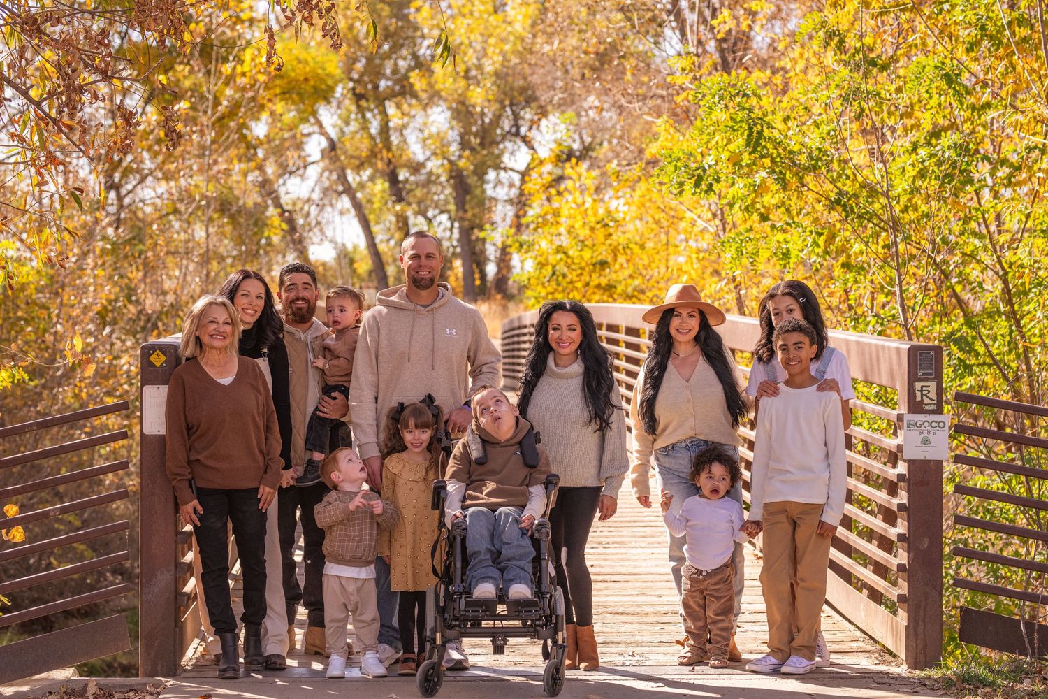 Large family group posing together on wooden bridge during autumn with colorful foliage.