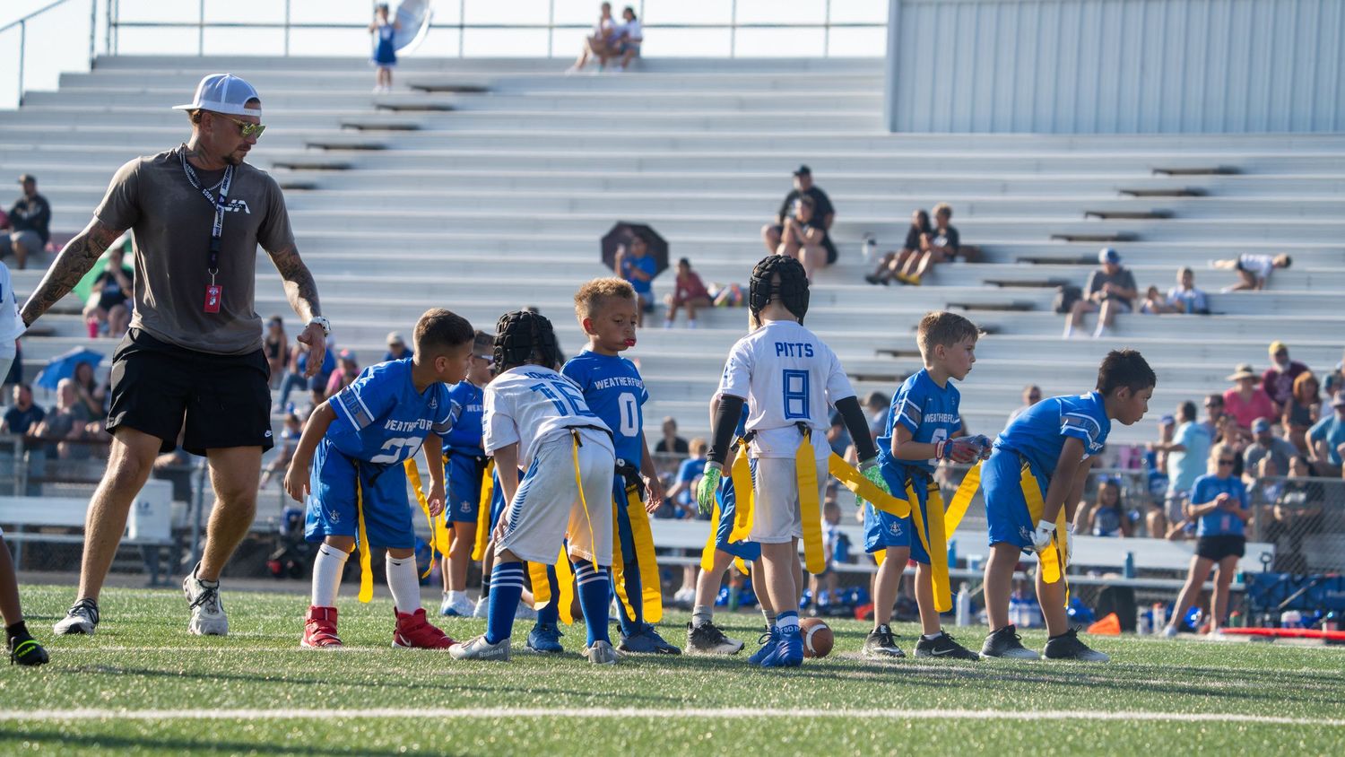 Wide panoramic view of athletes resting on a soccer field with stadium bleachers in the background.