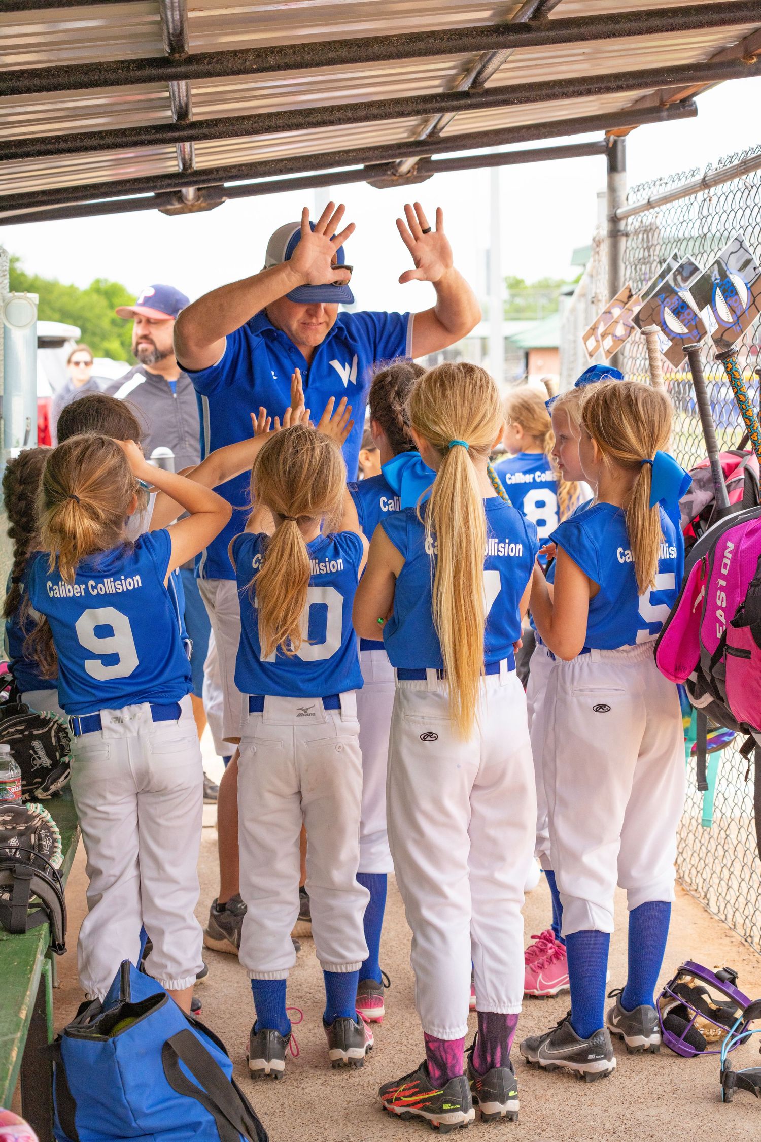 Youth softball team gathers in dugout with coach giving encouragement before game.