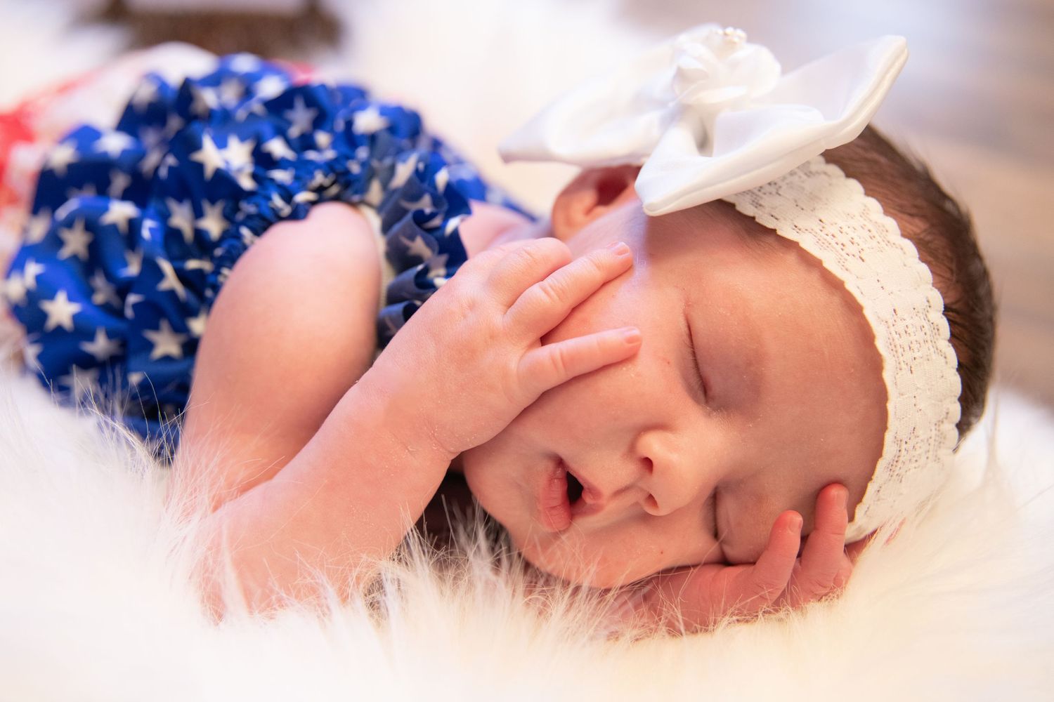 Sleeping newborn wearing a blue and white headband on soft white fabric.