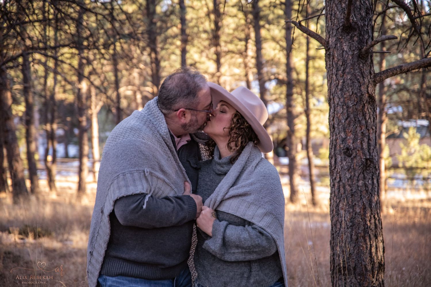 Intimate moment between two people sharing blanket in winter forest setting at sunset.
