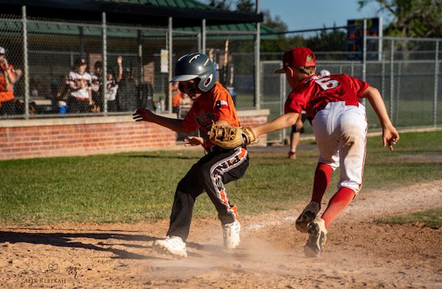 Baseball players in action during intense play at home plate with dust flying.