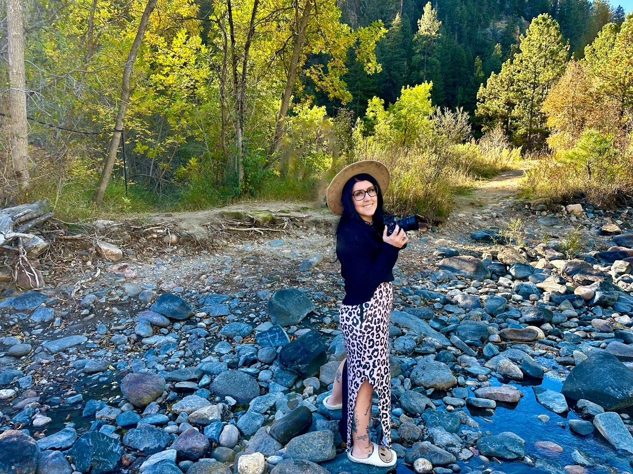 Casual outdoor portrait by rocky riverbed with autumn trees in background.