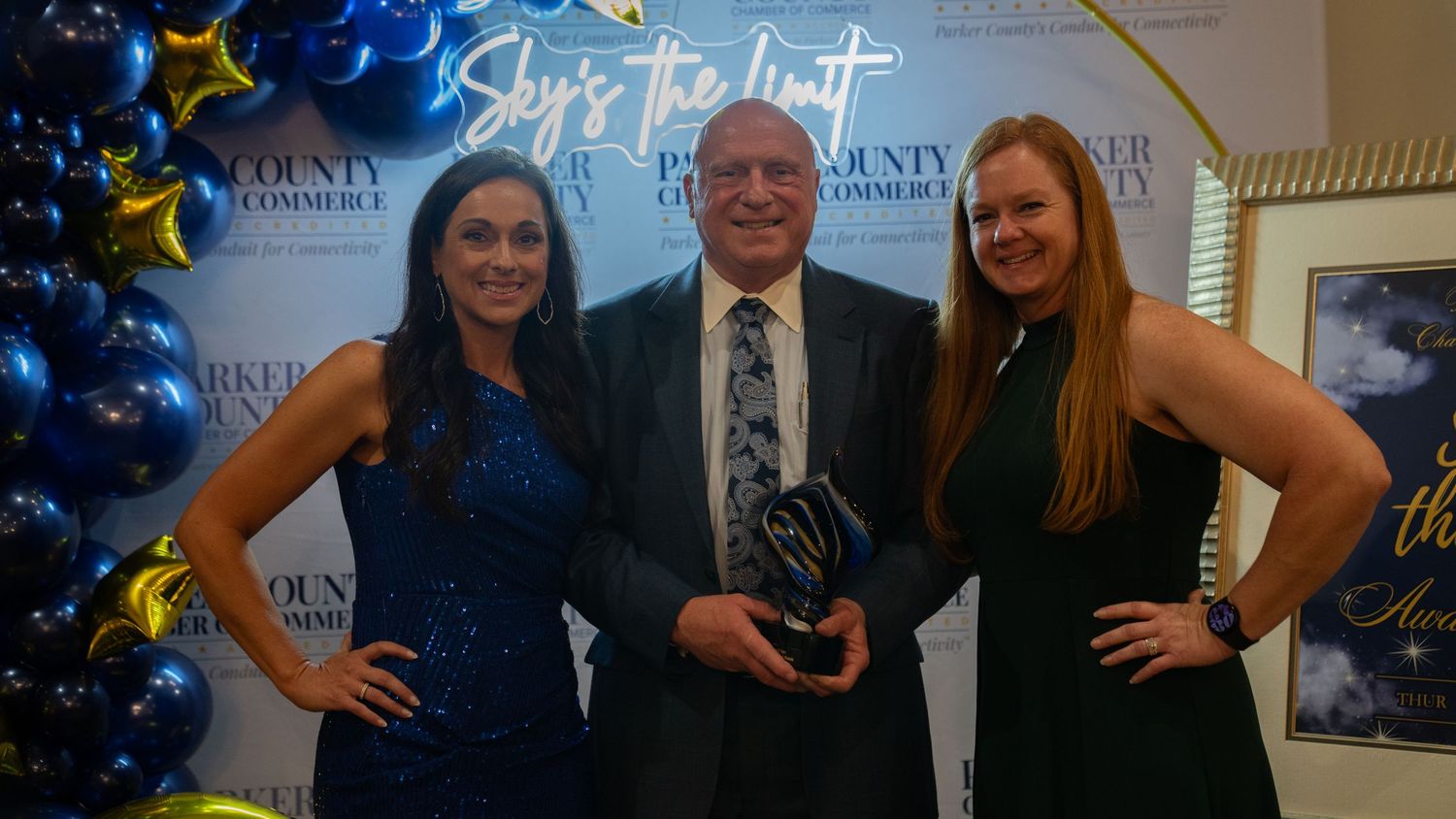 Award recipients pose with their trophy in front of a blue and gold balloon display.