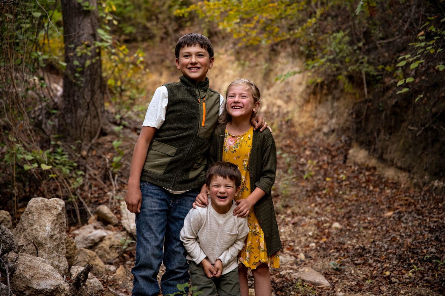 Three children posing together on rocky autumn trail in nature.