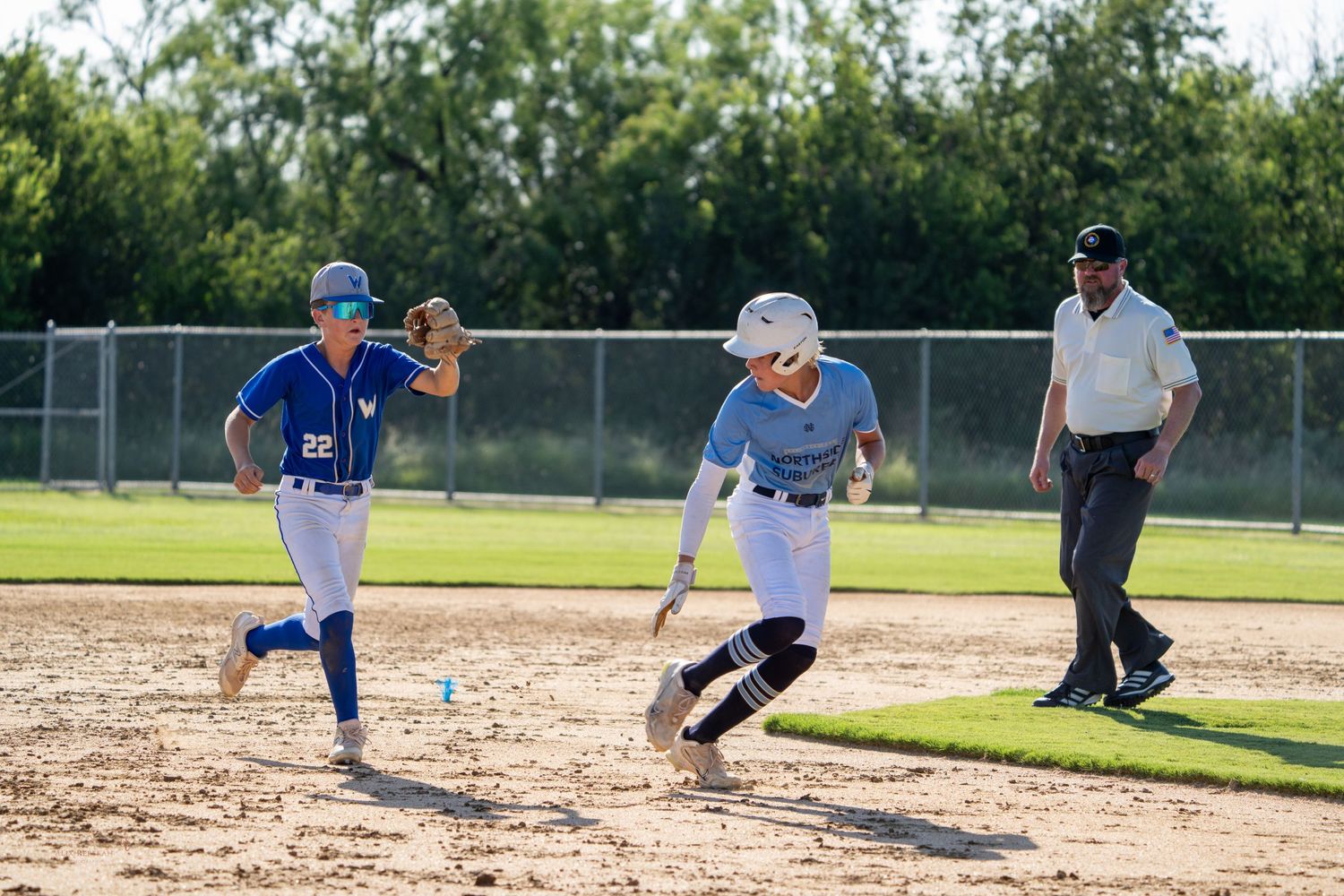 Baseball players running on dirt field during game with umpire watching.