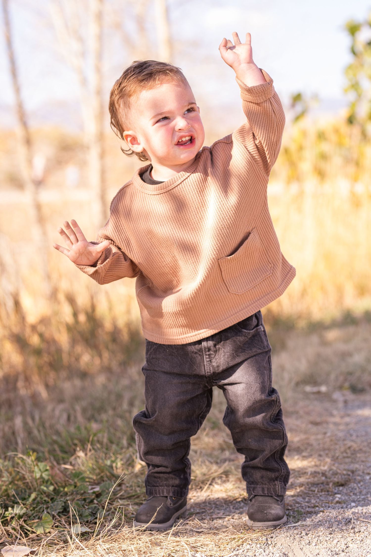 Excited child in beige sweater jumping and playing outdoors.