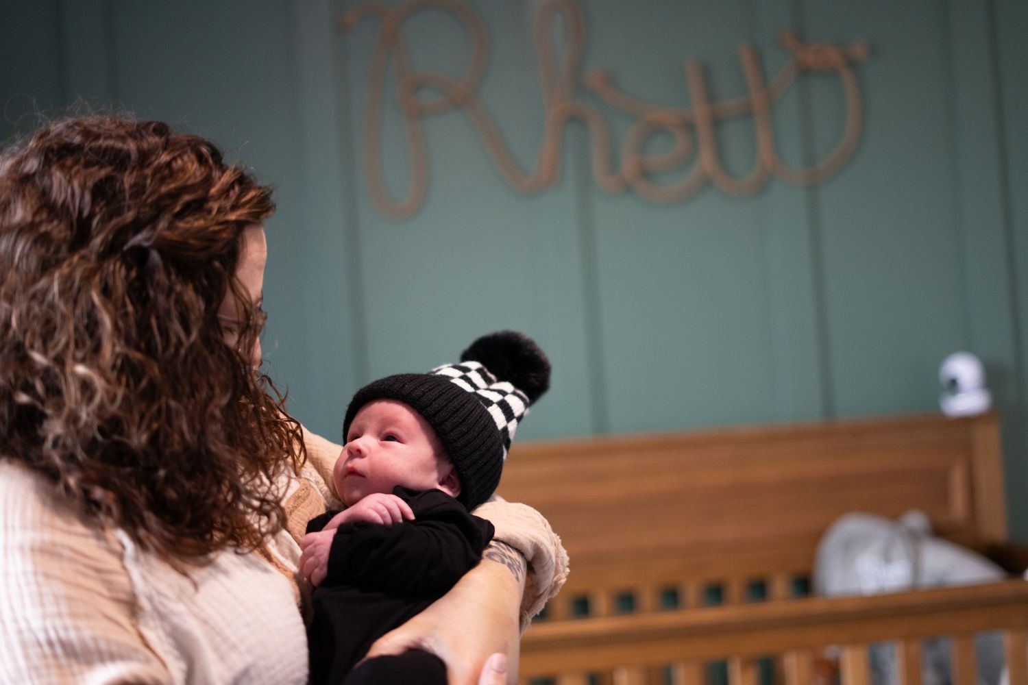 A parent cradles and gazes lovingly at a bundled infant wearing a winter hat in a nursery setting.