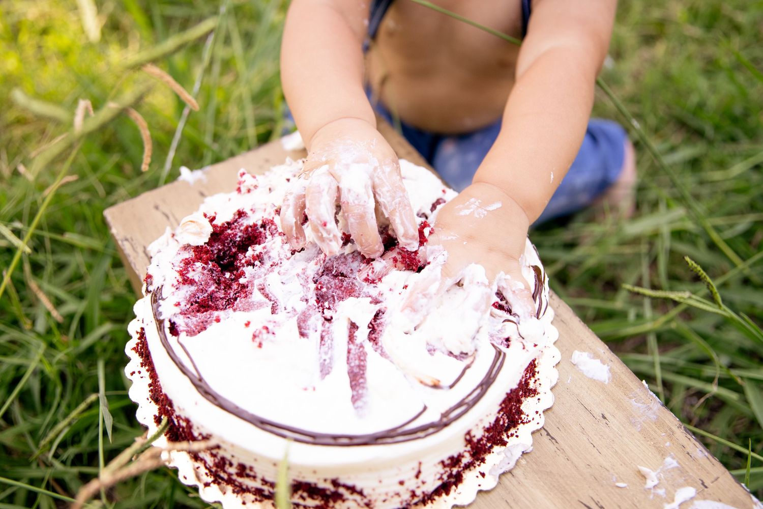 Small hands smashing into white frosted cake during an outdoor cake smash session.